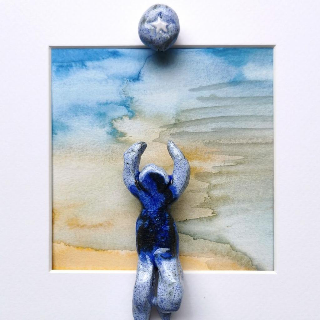 "Strandurlaub" 9/2025, 10,5 x 4 x 3,3 cm, schwarzer und weißer Ton glasiert mit Tonperle auf Aquarell, gerahmt (25 x25 cm)